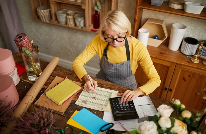 High angle portrait of female businesswoman counting finances using calculator in small shop, copy space