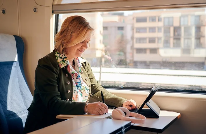Woman works from a train with a tablet and a notebook. Working remotely, travel