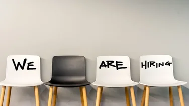 4 chairs (3 white one black) with we are hiring written across them
