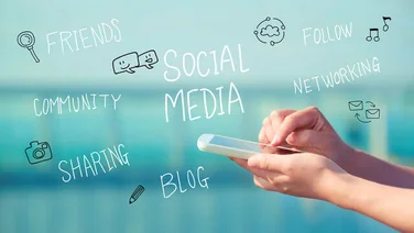 social media related words on a glass screen with hands typing on a mobile in front