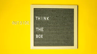 Black square board on a yellow background with the text "Think outside the box"