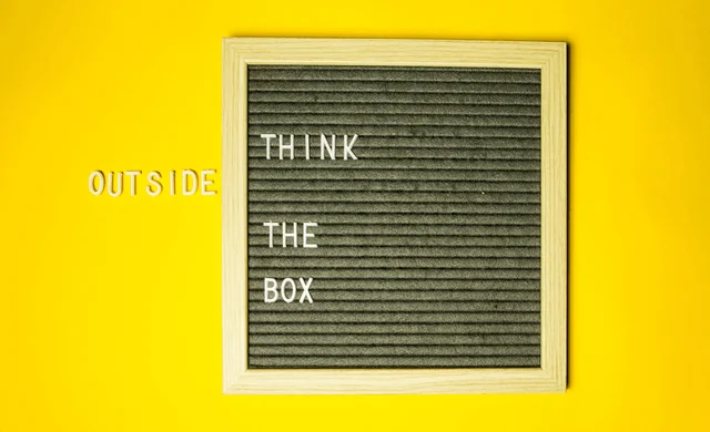 Black square board on a yellow background with the text "Think outside the box"
