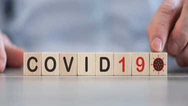 Mid shot of man behind a desk with COVID19 spelled out in wooden blocks