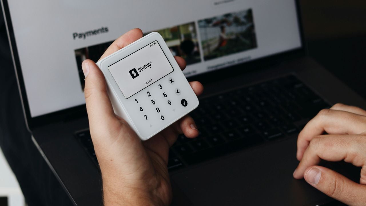 A hand holds the SumUp Solo Lite card reader in front of a terminal. 