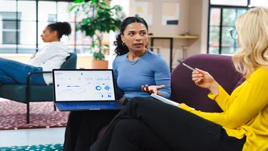 A woman shows her laptop screen to a colleague during a meeting