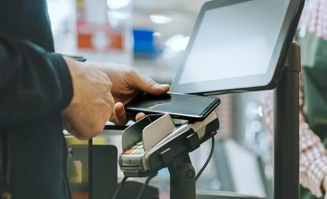 Close up of a mobile phone tapping a card reader to make payment in a shop