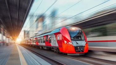 Electric passenger train drives at high speed among urban landscape.