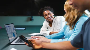 A smiling woman talks to her colleague in front of a laptop