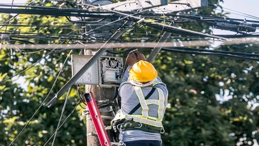 A technician on a ladder fixes a pole mounted fiber optic terminal splitter box to repair or restore internet connection to nearby houses.