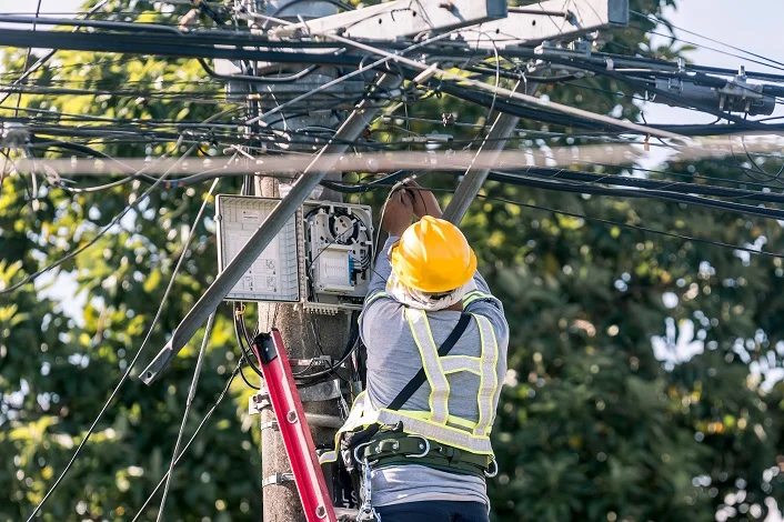 A technician on a ladder fixes a pole mounted fiber optic terminal splitter box to repair or restore internet connection to nearby houses.