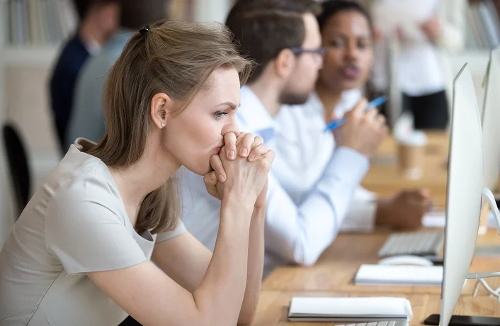 Upset frustrated and confused female worker folding hands on chin feels puzzled having problem troubles and doubts about business moments, sitting in shared modern office with multinational coworkers