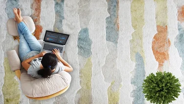 Overhead shot of a young woman working on a laptop whilst sat on a stripey multicoloured carpet