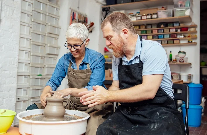 Photo of an apprentice and an older woman mentor sitting at a pottery wheel in an East London studio
