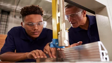 Carpenter Training Male Apprentice To Use Mechanized Saw