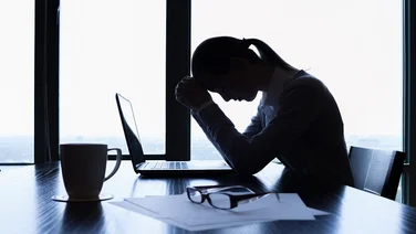 Stressed business woman sits in front of a laptop at an office desk with her head in her hands