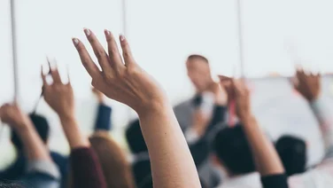 Audience raising hands up while businessman is speaking in training at the office.
