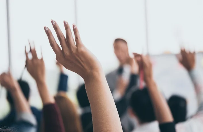 Audience raising hands up while businessman is speaking in training at the office.