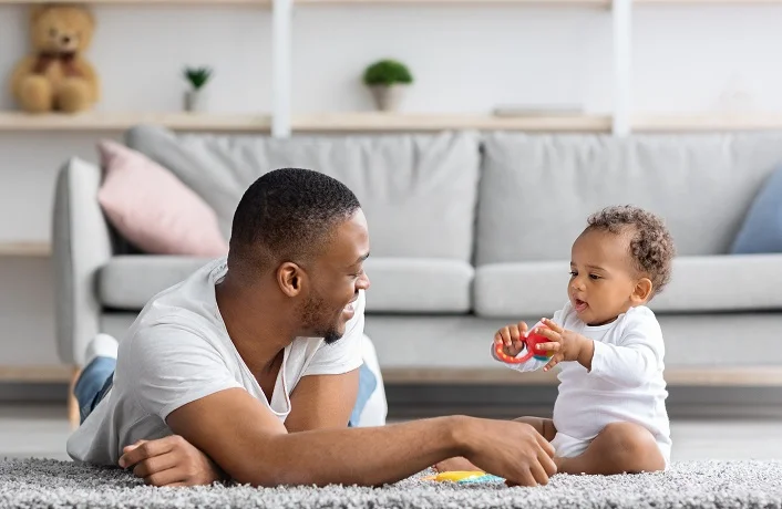 Shared Parental Leave. Young Black Father Playing With Little Baby At Home