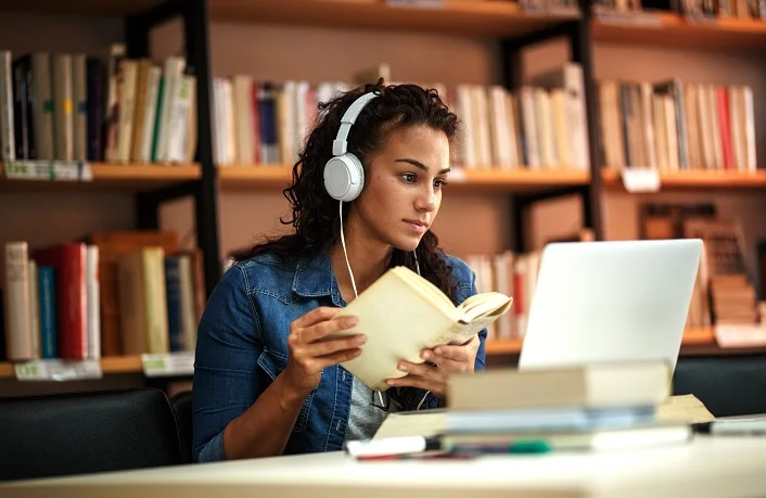 Young female student studies in the library using a laptop