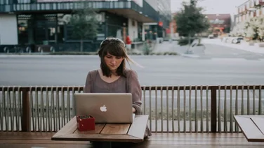 a woman works at a laptop at a roadside cafe