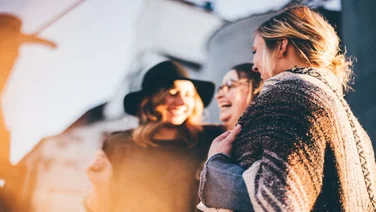 three women share a joke while standing in the sunlight