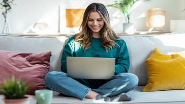 Shot of woman working with laptop while sitting on couch in living room at home