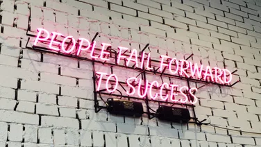 Neon sign reading "People Fail Forward To Success" comfortable with failure