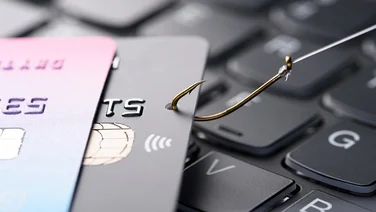 Credit card on fishing hook pulled from stack on keyboard, phishing scam data theft concept