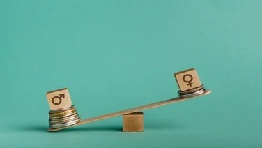 Gender pay gap. Wooden cubes with male and female gender signs on seesaw with different stacks of coins, men outweigh, copy space