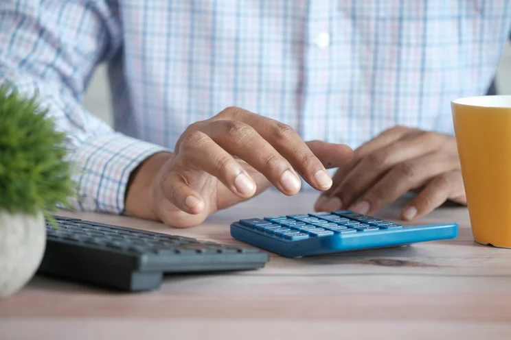 Small business owner using blue calculator to calculate payroll at desk