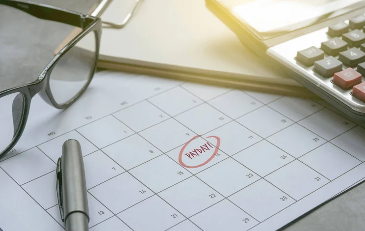 Calendar with payday circled in red, surrounded by glasses, pen, and calculator