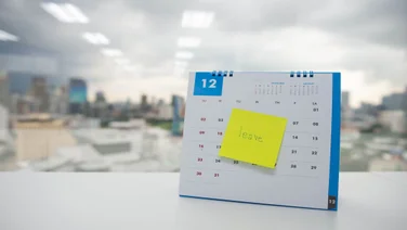 Calendar on an office desk, blocked out with a post-it note reading "Leave"