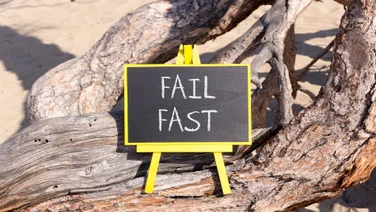 A blackboard sign sitting on a tree that reads "Fail Fast"