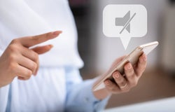 A shot of a pair of hands with one holding a white phone, with a no sound notification bubble above.