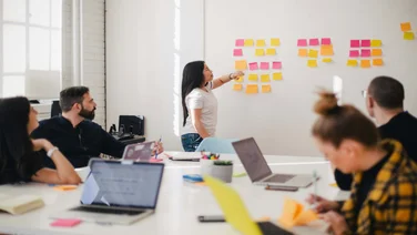 Team meeting with leader presenting by white board with post it notes.