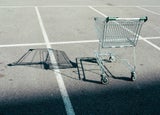 An empty shopping cart casts a shadow over an empty car park