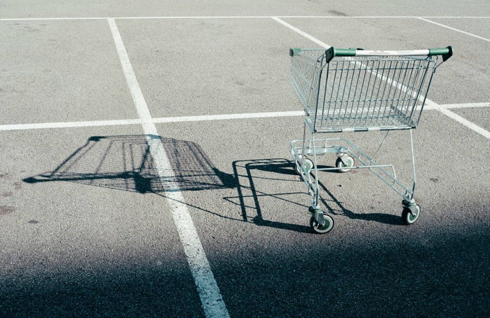 An empty shopping cart casts a shadow over an empty car park