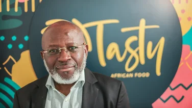 Image of Michael Olaleye, founder and managing director of Tasty African Food, in front of a blurred sign reading Tasty African Food