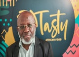 Image of Michael Olaleye, founder and managing director of Tasty African Food, in front of a blurred sign reading Tasty African Food