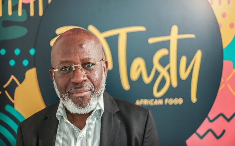 Image of Michael Olaleye, founder and managing director of Tasty African Food, in front of a blurred sign reading Tasty African Food