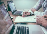 Two colleagues complete paperwork in front of their laptops