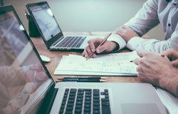 Two colleagues complete paperwork in front of their laptops