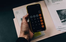 A hand holds a smartphone with a the calculator app open.