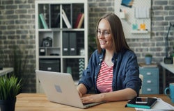 A smiling woman sits working at her laptop.