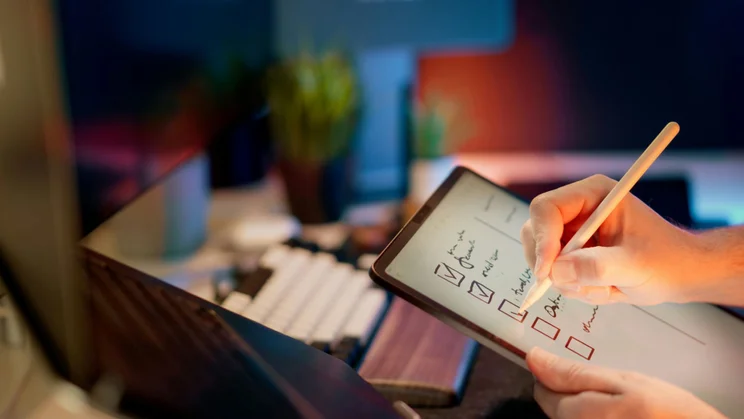 A person ticks of a list of items on a tablet at their desk.