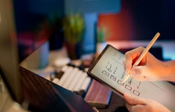 A person ticks of a list of items on a tablet at their desk.