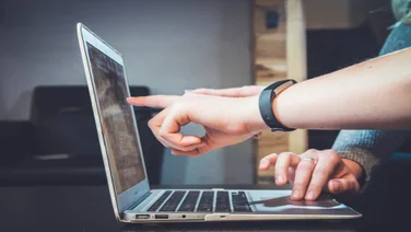 Two pairs of hands are gesturing and pointing towards a laptop screen.