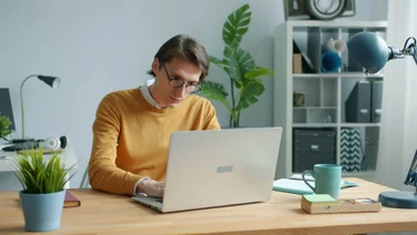 A man sits in a home office working on his laptop.