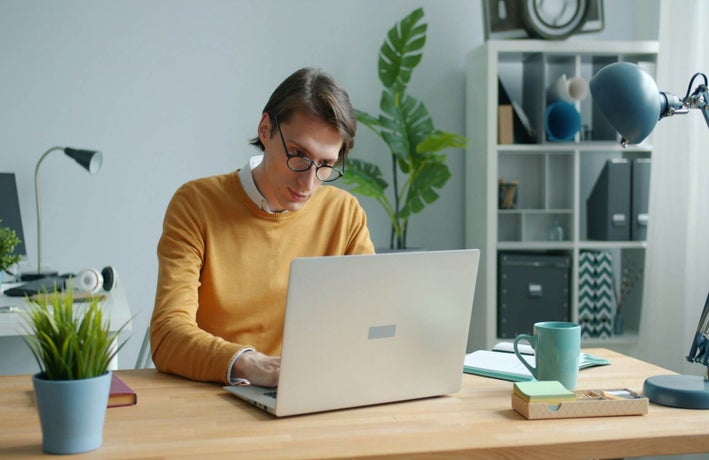 A man sits in a home office working on his laptop.