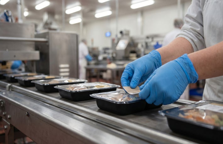 Worker putting a label on food on a factory line